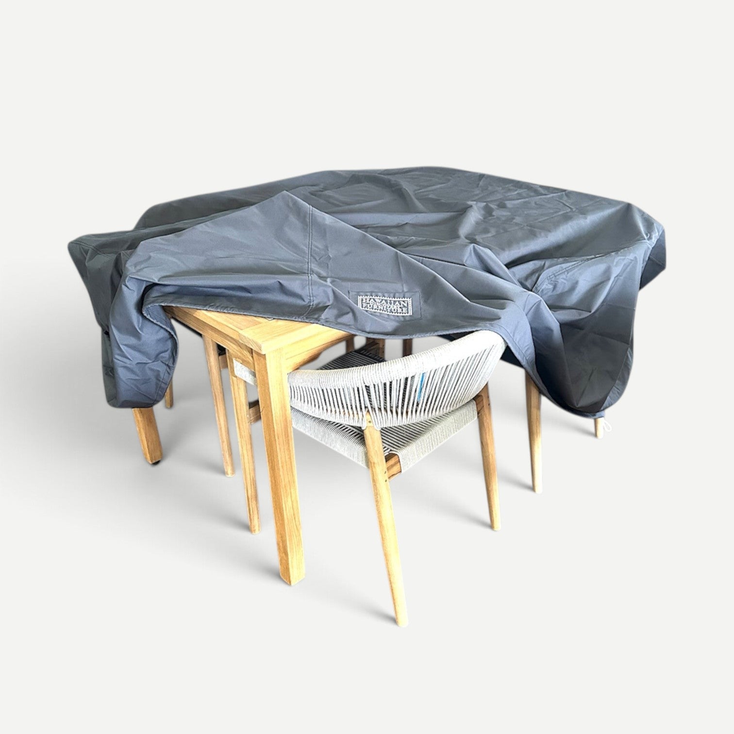 Hawaiian Discovery Furniture water-resistant grey polyester cover draped over a teak Anna dining table and chair set