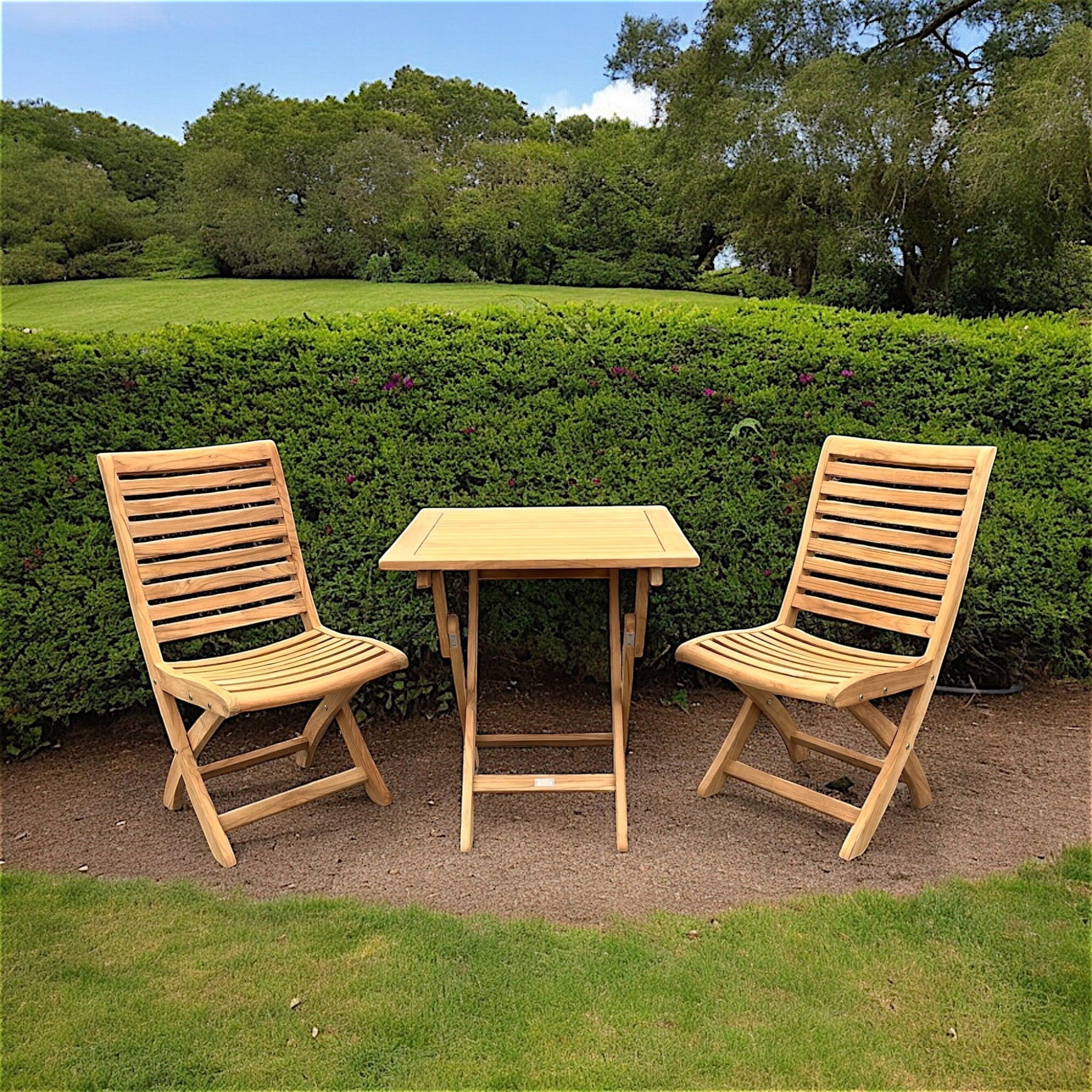 Hawaiian Discovery Furniture Kakahiaka set with two teak folding chairs and a square folding table in a garden.