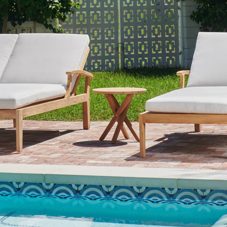 Hawaiian Discovery Furniture Tulum teak side table with crossed-leg design placed between two outdoor lounge chairs.