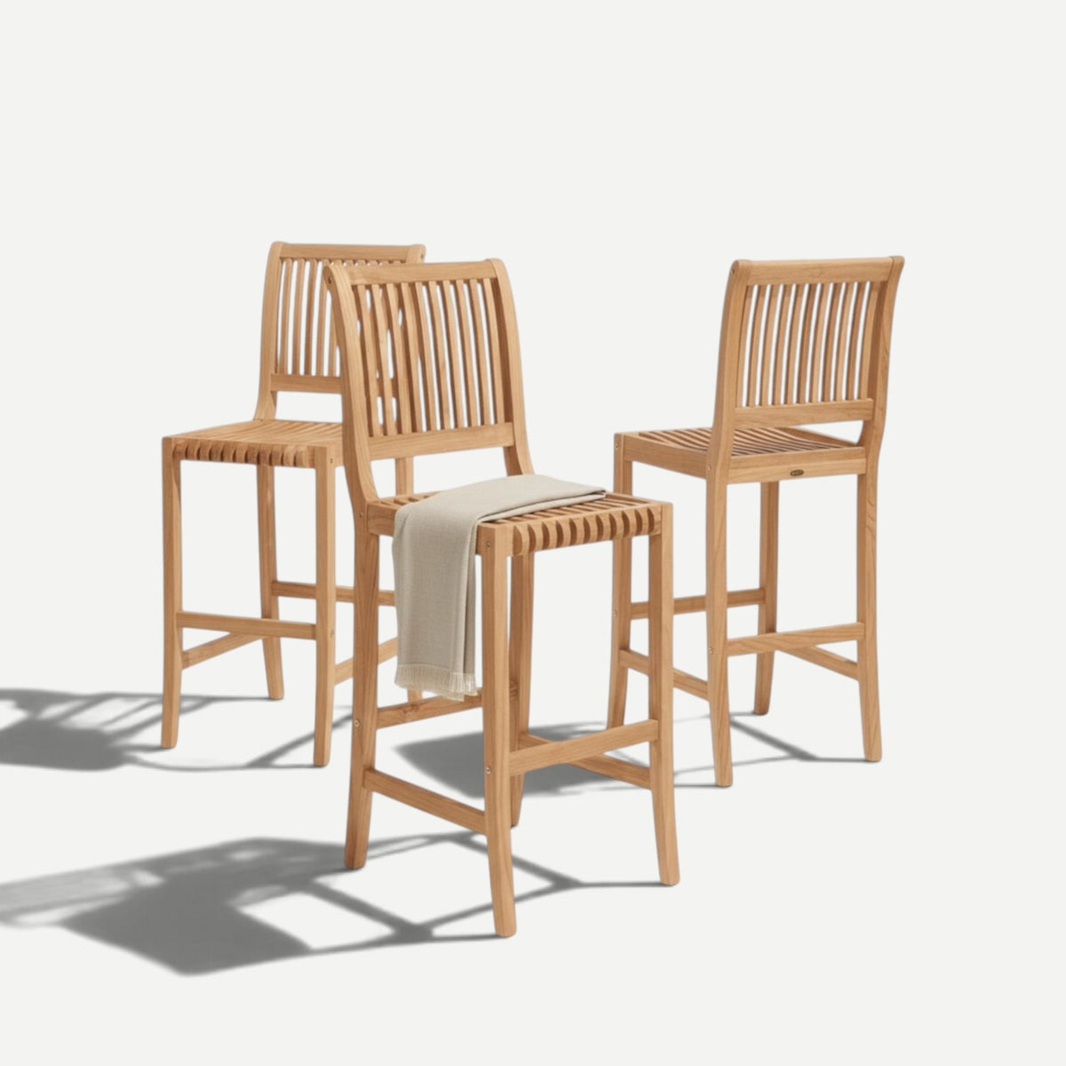 Three Hawaiian Discovery Furniture Palm high teak bar chairs with slatted backs and a beige throw blanket.