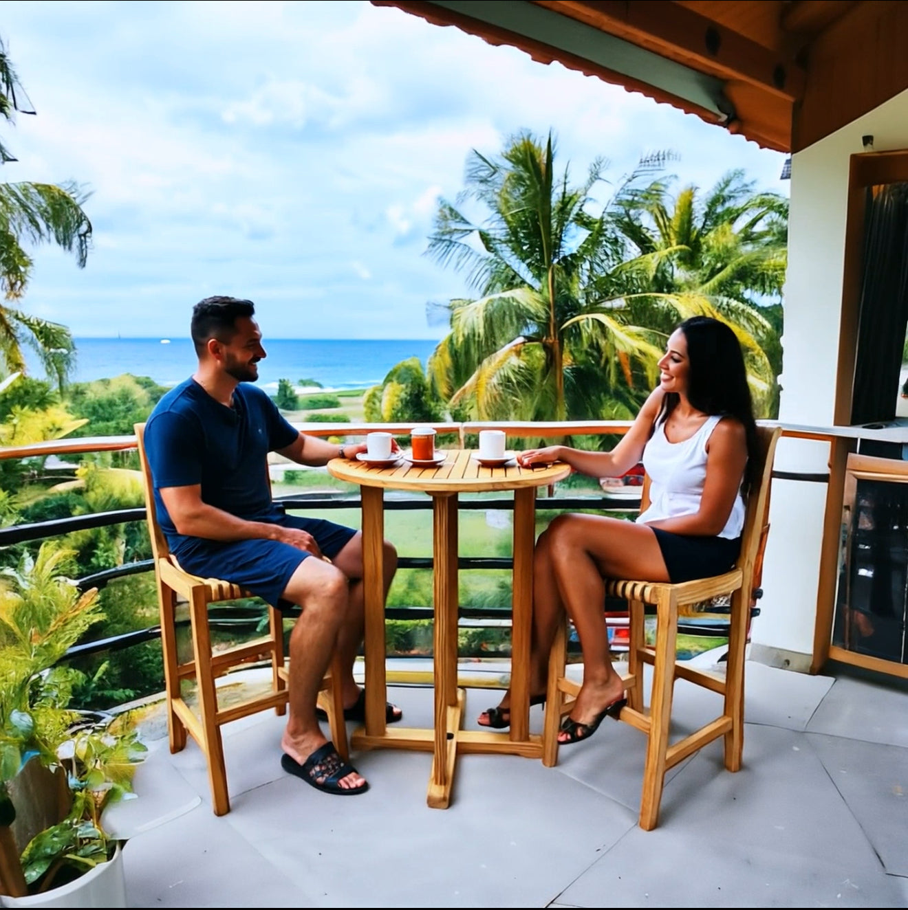 Hawaiian Discovery Furniture Palm High Bar Set with a couple sitting at a round teak table on a tropical balcony