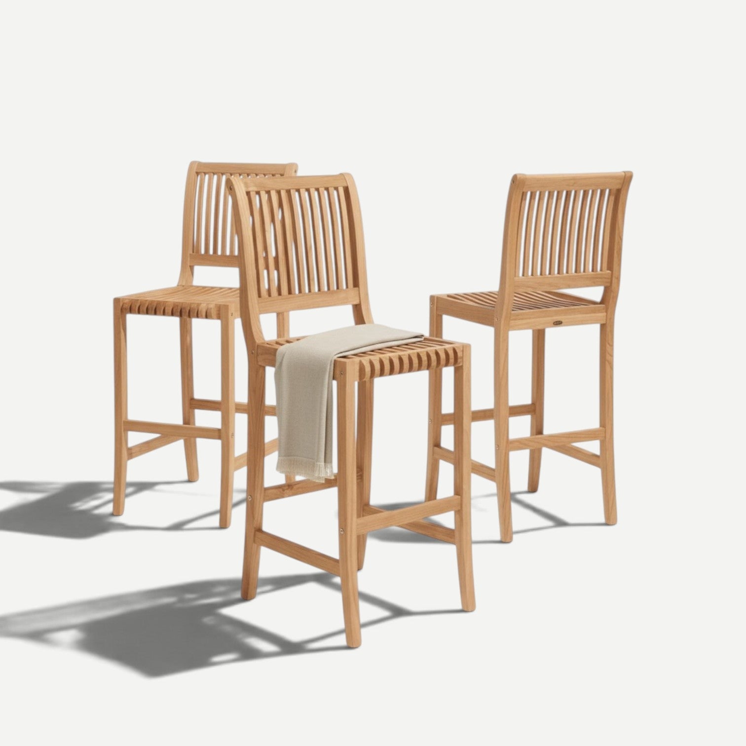 Hawaiian Discovery Furniture Palm high bar stools made of solid teak wood with curved slats and a light beige throw.