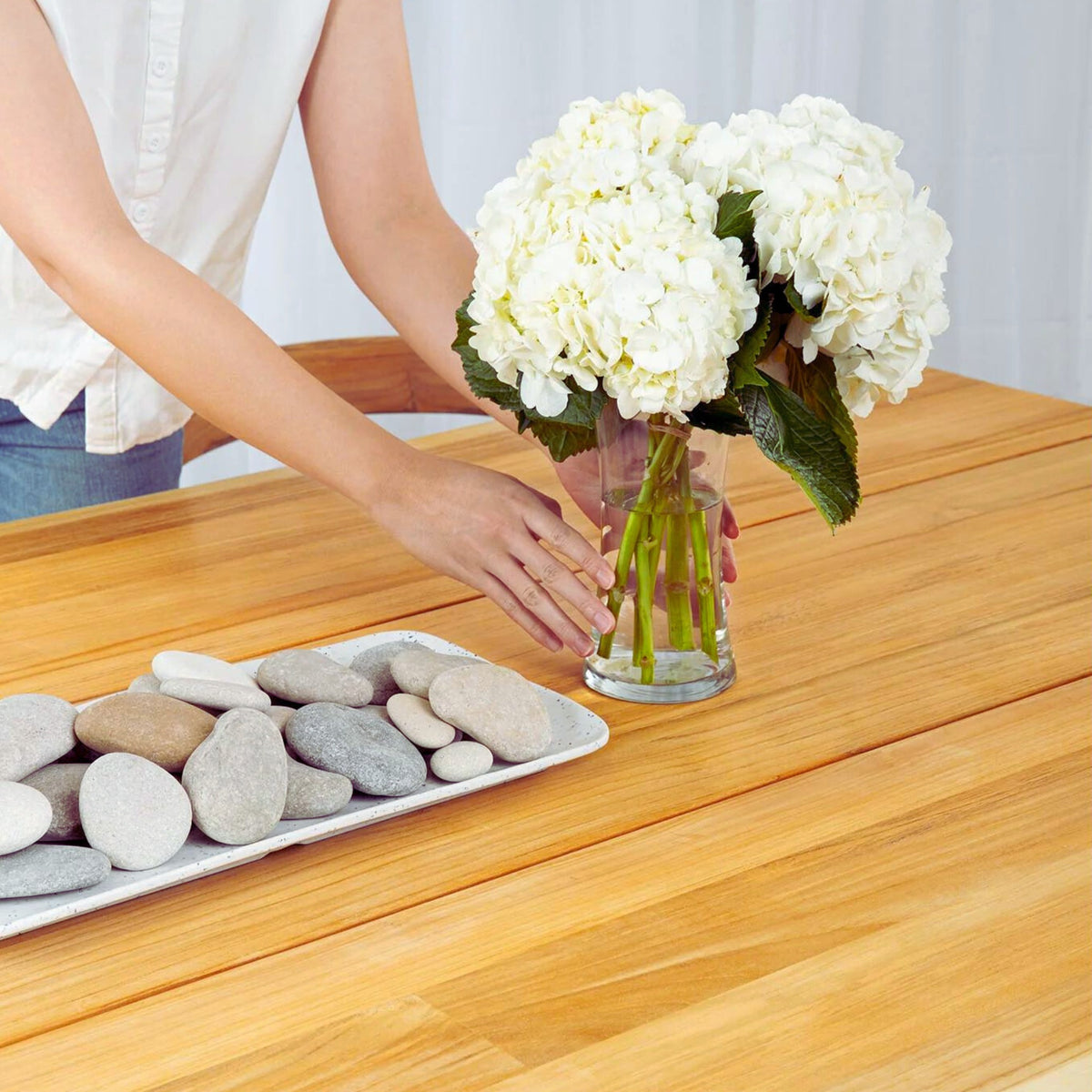 Hawaiian Discovery Furniture La Costa teak dining table with a person placing a vase of white hydrangeas on top