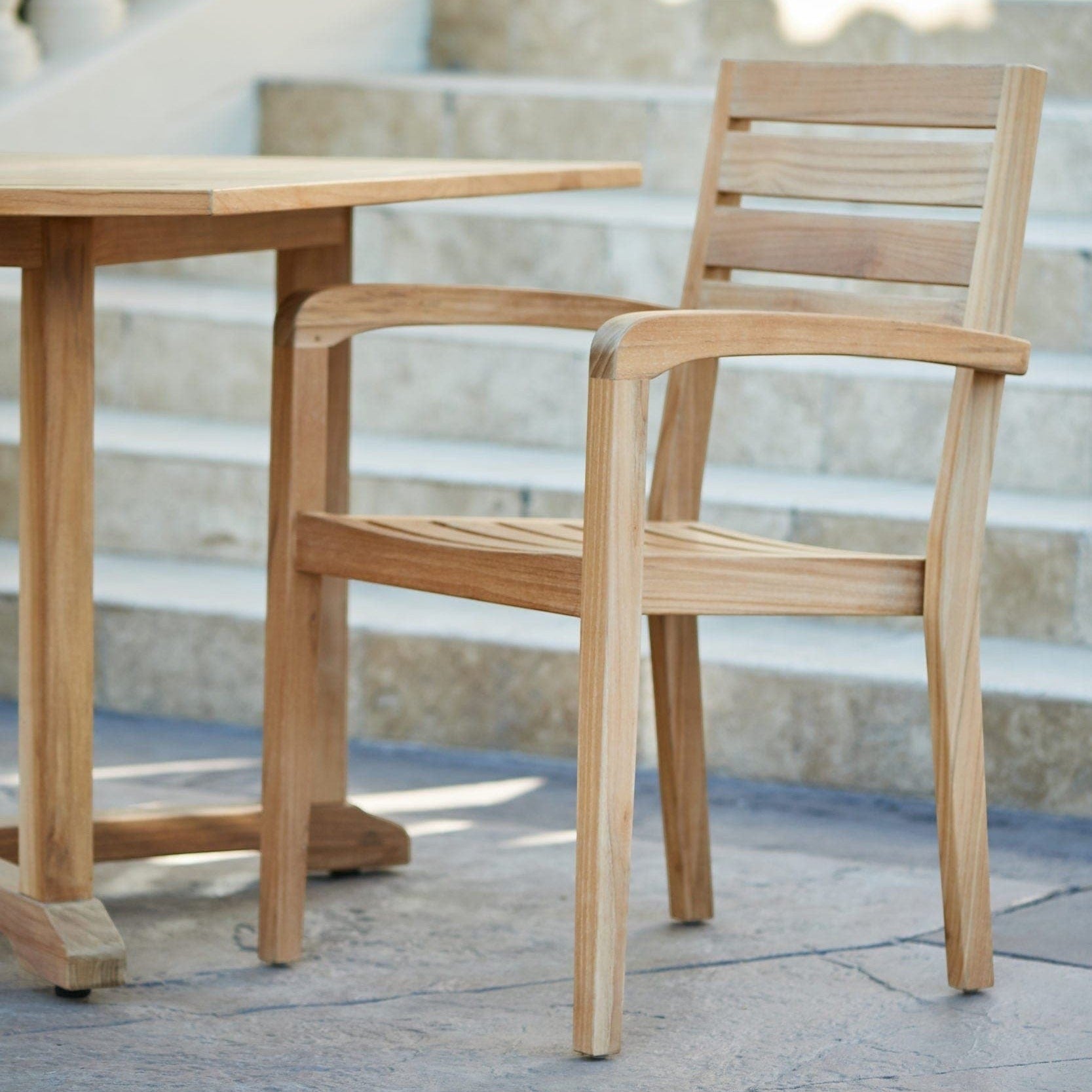 Hawaiian Discovery Furniture Venice teak outdoor arm chair with a natural honey finish on a stone patio.